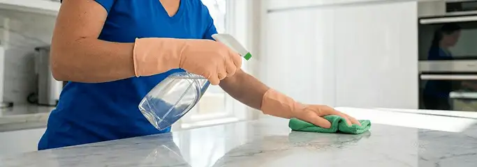 Maid service worker spraying and wiping a kitchen countertop with a microfiber cloth for sanitizing, Lincoln, NE.