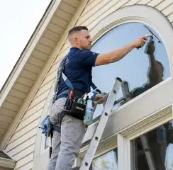 Professional window cleaner on a ladder using a squeegee to clean an exterior arched window, Lincoln, NE.