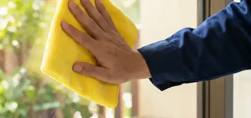 House cleaner wiping a glass window with a yellow microfiber cloth for streak-free cleaning, Lincoln, NE.